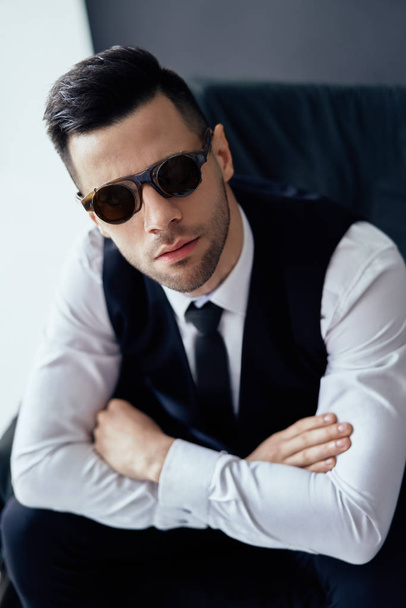 Handsome elegant man in retro sunglasses posing in studio on black background - Fotó, kép