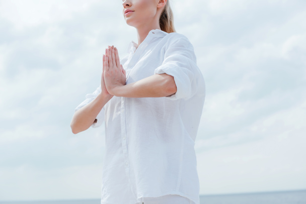vista cortada da mulher de pé com as mãos orando perto do mar
  - Foto, Imagem