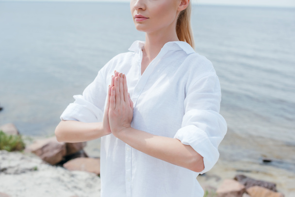 abgeschnittene Ansicht einer jungen Frau mit betenden Händen in der Nähe des Meeres  - Foto, Bild
