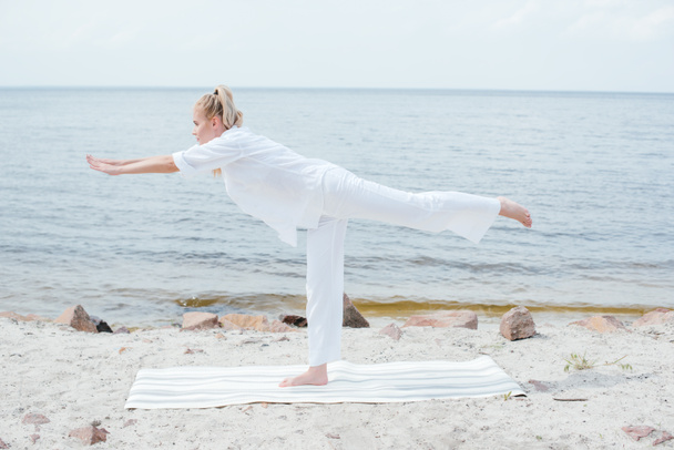 vista lateral de una joven rubia haciendo yoga cerca del mar
  - Foto, imagen