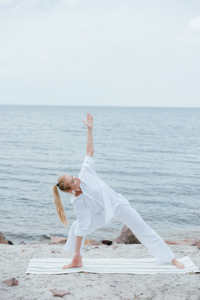 pretty girl with closed eyes practicing yoga on yoga mat near sea  - Foto, Imagem