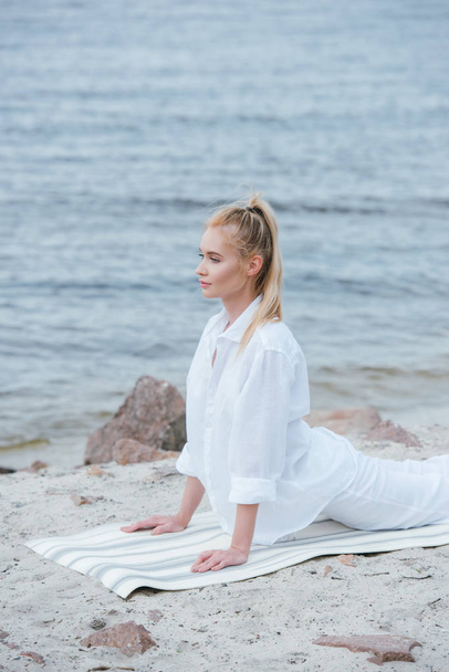 schönes Mädchen praktiziert Yoga auf Yogamatte in Flussnähe  - Foto, Bild