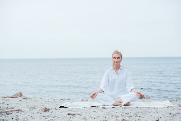 счастливая блондинка с закрытыми глазами сидит на коврике для йоги
  - Фото, изображение