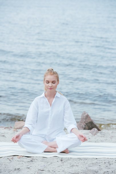 jovem loira pacífica com olhos fechados praticando ioga perto do rio
  - Foto, Imagem