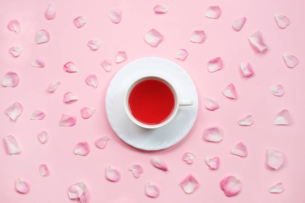 obere Ansicht einer Tasse Tee, umgeben von niedlichen rosa Rosenblättern auf pastellrosa Hintergrund. flach lag. Stillleben mit Teetasse. - Foto, Bild