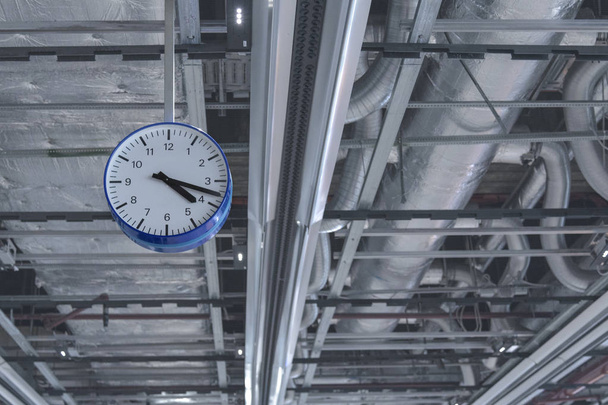 View of the clock that hangs from the ceiling against the background of ventilation pipes. - Photo, Image