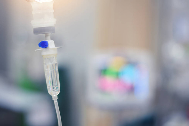 IV infusion set and bottle on a pole. Liquid saline is slowly dripping drops of drugs, medicine or antibiotic therapy and surgery recovery in a hospital or clinic ,soft focus - Фото, изображение