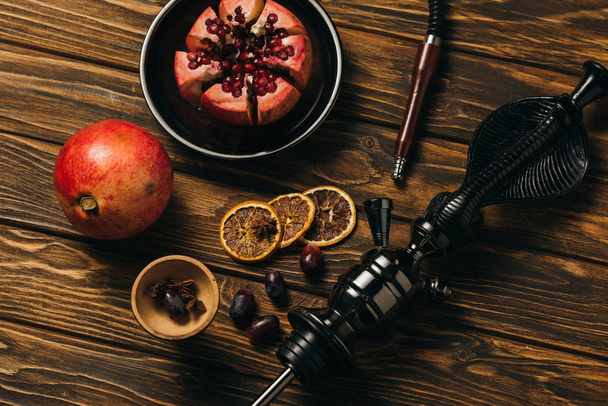 top view of hookah, garnets, grapes and dried cut oranges on wooden surface - Fotografie, Obrázek