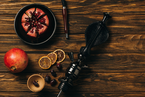 top view of hookah, garnets, grapes and dried cut oranges on wooden surface - Fotó, kép