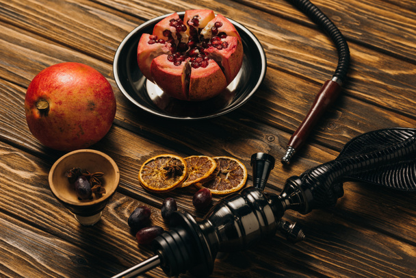 hookah, garnets, grapes and dried cut oranges on wooden surface - Foto, afbeelding
