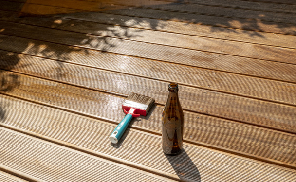 botella de cerveza vacía y un cepillo están tumbados en la terraza medio empotrada con esmalte
 - Foto, Imagen