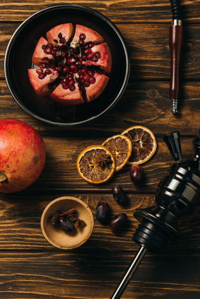 top view of garnets, grapes, dried cut oranges and hookah on wooden surface - Foto, Imagen