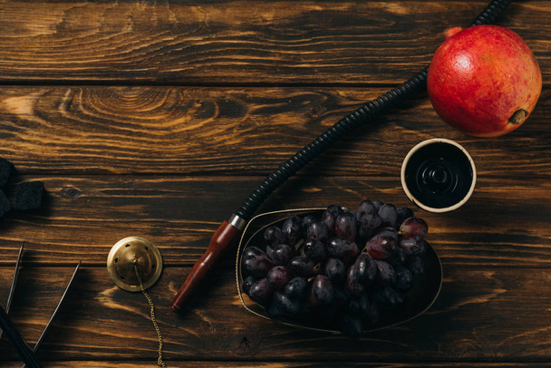 top view of hookah, grapes, garnet and coals on wooden surface - Fotografie, Obrázek