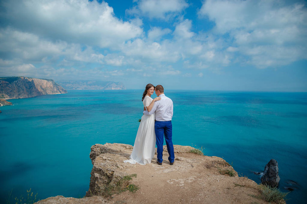 Beautiful couple on the sea rocks in wedding dress. Just married view from behind. - Fotó, kép