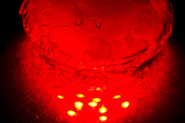 a glass hookah flask filled with bubbling water and smoke glows in the dark in red. luminescence in darkness - Photo, Image