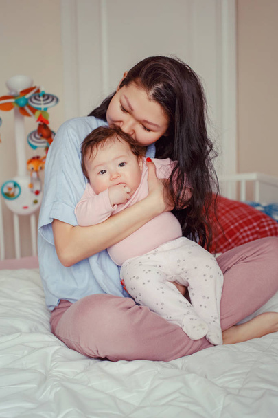 Portrait of beautiful mixed race Asian mother kissing touching embracing her cute adorable newborn infant baby. Early development and health care lifestyle concept. Family in bedroom - Foto, imagen