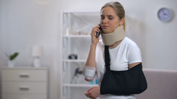 Displeased woman in foam cervical collar and arm sling talking phone, bad news - Footage, Video