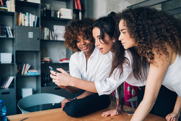 trzech wielorasowych młodych przyjaciół patrzących na smartfona w nowoczesnym współpracowniku - Zdjęcie, obraz