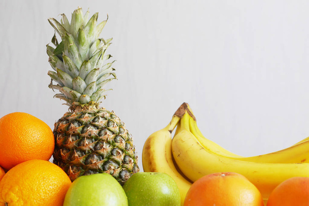fresh fruit pile, pineapple, oranges, apples and bananas on gray background - Foto, afbeelding