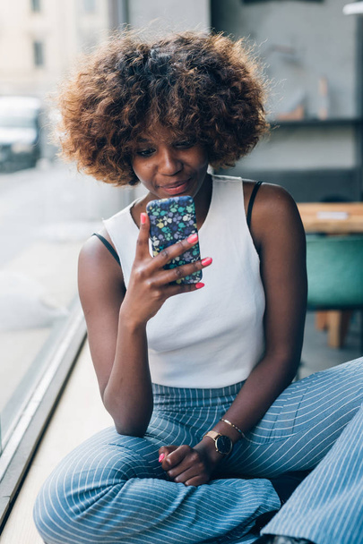 mujer africana joven usando teléfono inteligente y relajante
  - Foto, Imagen