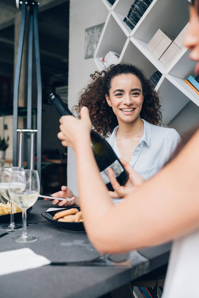 dos mujeres caucásicas jóvenes bebiendo vino en restaurante moderno y celebrando
 - Foto, Imagen