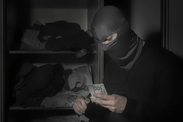 Dief in een masker met een mes en met een zaklamp steelt geld  - Foto, afbeelding