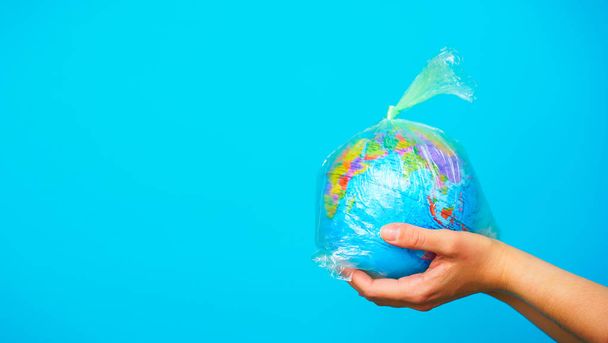 Woman holds in hands plastic bag with planet earth at blue background. The concept of plastic pollution. - Valokuva, kuva