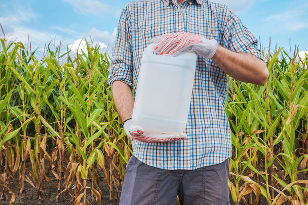Farmer holding unlabeled pesticide jug in field - 写真・画像