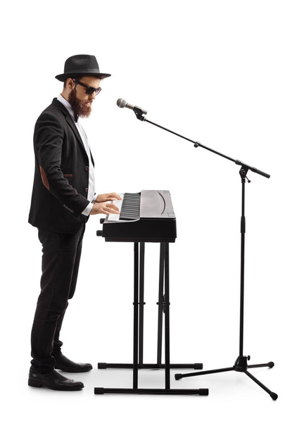 Full length shot of a man standing, playing a digital piano and singing on a microphone isolated on white background - Foto, Imagem