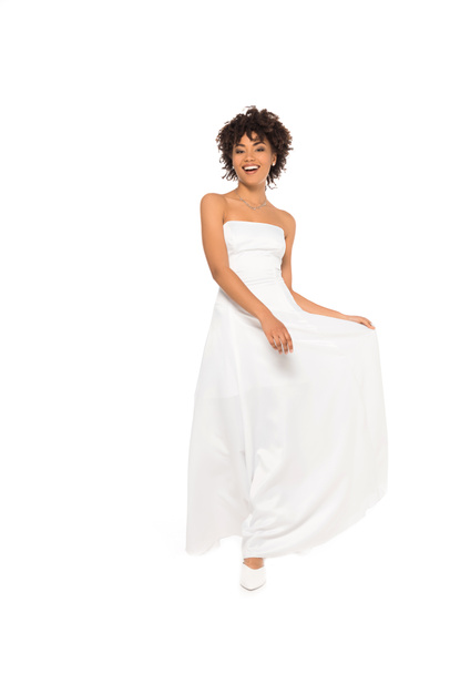 happy african american bride smiling while touching wedding dress isolated on white  - Photo, image