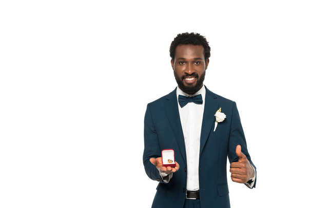 cheerful african american man holding box with wedding ring and showing thumb up isolated on white  - Fotografie, Obrázek