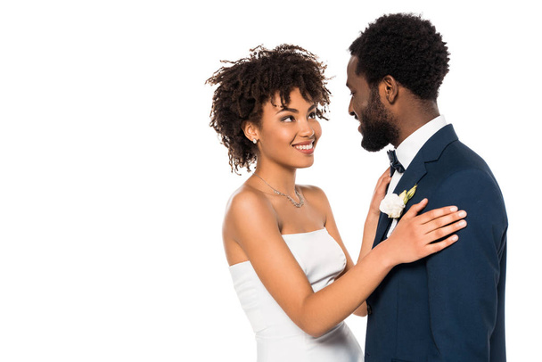 Veselý afroamerický ženich, který se dívá na nevěstu, zatímco se objímá izolovaně na bílém  - Fotografie, Obrázek
