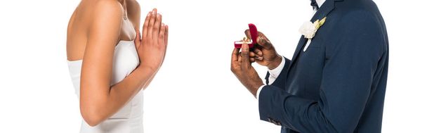 πανοραμική βολή του αφρικανικού αμερικανικού άντρα κρατώντας κουτί με δαχτυλίδι, ενώ κάνει πρόταση σε γυναίκα απομονωθεί σε λευκό  - Φωτογραφία, εικόνα