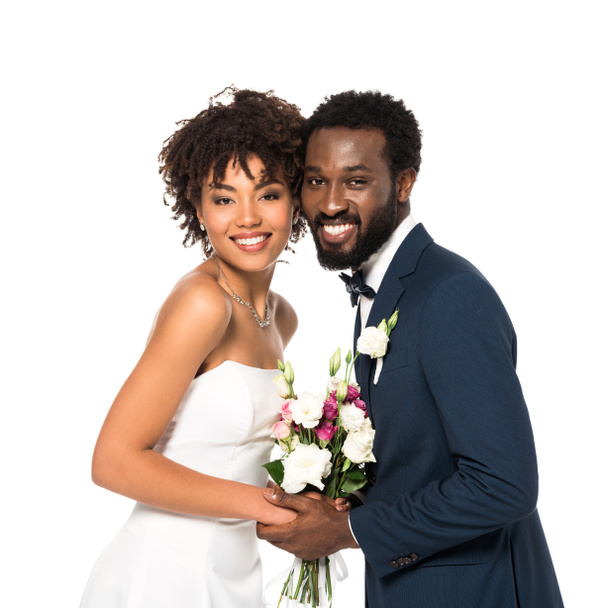 幸せなアフリカ系アメリカ人の花嫁と花婿は花束を持ち、白で隔離されたカメラを見て  - 写真・画像