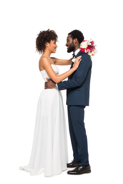 happy african american bride holding flowers and looking at bearded bridegroom isolated on white - Foto, Bild