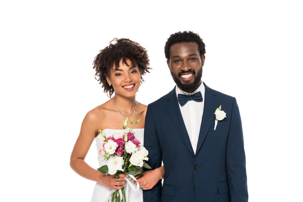joyeuse mariée afro-américaine tenant des fleurs près du marié en regardant la caméra isolée sur blanc
 - Photo, image