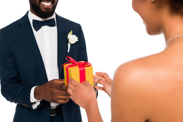 bijgesneden weergave van Happy African American bruidegom geven geschenk aan krullend bruid geïsoleerd op wit  - Foto, afbeelding