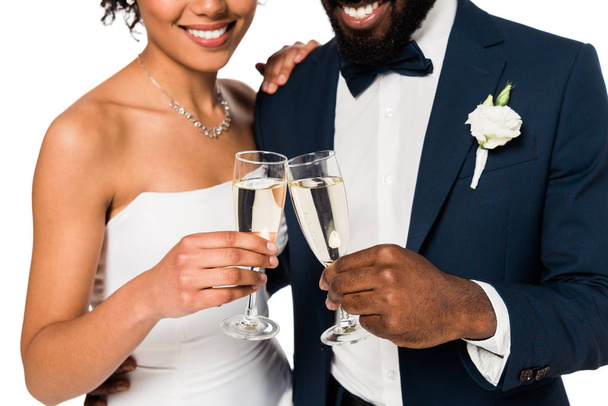 κομμένη θέα της ευτυχισμένη αφρικανική Αμερικανίδα νύφη και γαμπρός κουδουνίσασαμπάνια γυαλιά απομονώνονται σε λευκό  - Φωτογραφία, εικόνα