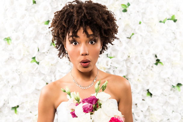 surprised african american bride looking at camera while holding flowers  - Fotó, kép