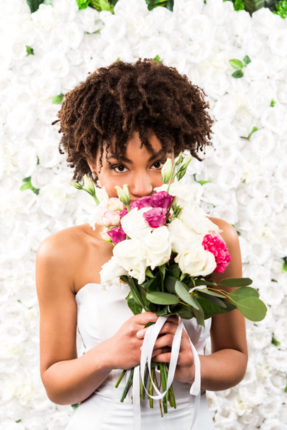 african american bride covering face while holding flowers  - Fotografie, Obrázek