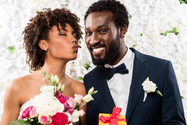 陽気な花婿の近くに花と花束を持つアヒルの顔を持つアフリカ系アメリカ人の花嫁 - 写真・画像