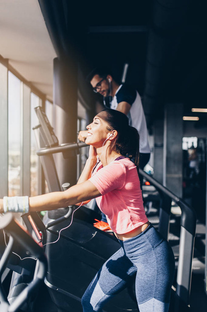 Young fit man and woman running on treadmill in modern fitness gym. - Photo, image