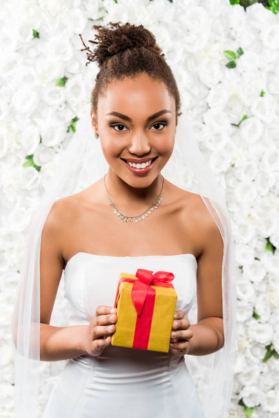 alegre noiva americana africana em véu segurando presente perto de flores
  - Foto, Imagem