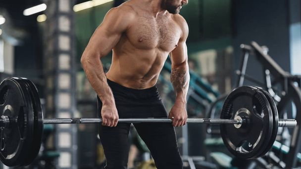 Сильный мужчина с обнаженным мускулистым телом, тренирующийся с тяжелой штангой
 - Фото, изображение