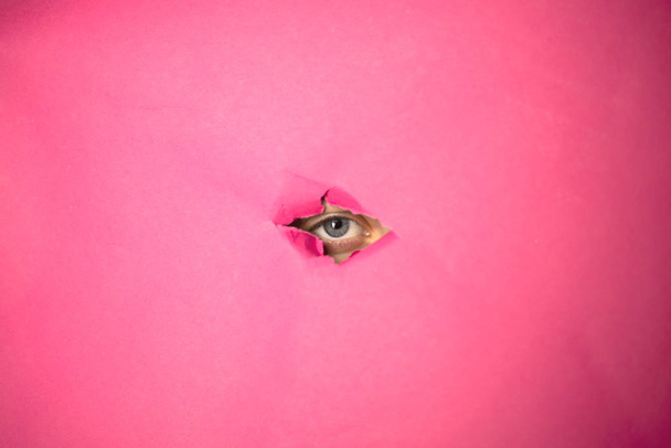 El ojo mira a través del agujero en papel rosa
 - Foto, imagen