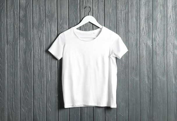 Hanger with white t-shirt on wooden background. Mockup for design - Fotó, kép