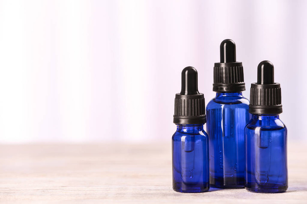 Bottles of essential oils on table against light background, space for text. Cosmetic products - Φωτογραφία, εικόνα