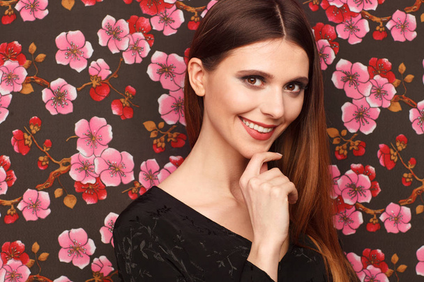 Portrait of a beautiful woman in a black dress. Background from a fabric in drawing flowers - Фото, зображення