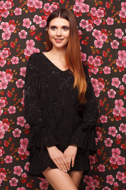 Portrait of a beautiful woman in a black dress. Background from a fabric in drawing flowers - Fotoğraf, Görsel