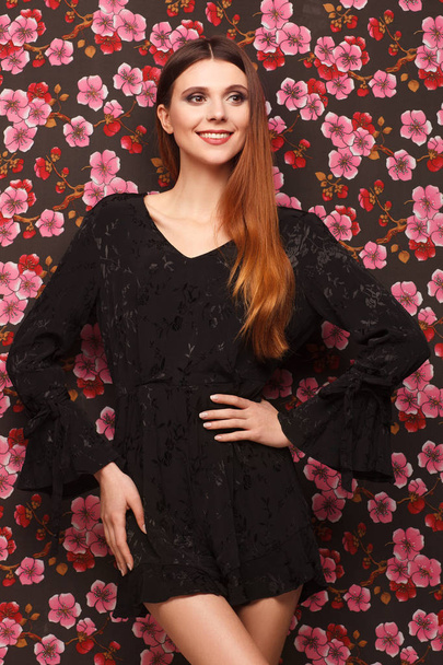 Portrait of a beautiful woman in a black dress. Background from a fabric in drawing flowers - Foto, Imagen